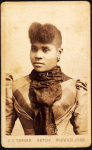 Half-portrait of young woman wearing large lace scarf over plaid bodice.
