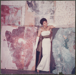Studio portrait of Nanette Rohan Bearden modeling an evening gown with a group of paintings