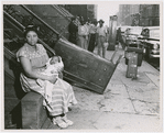 Woman with a baby sitting outside of building from which they had been evicted, in Harlem, New York