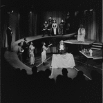 Godfrey Cambridge (in mask at table) and cast in the stage production The Blacks