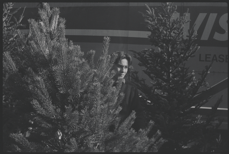 Black and white photo of a man standing between Christmas trees