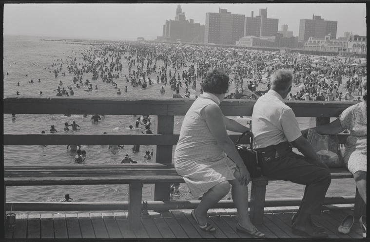 Couple sitting on a pier overlooking crowds at the beach