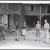 Group (5, with local boy walking on left) outside dilapidated house during performance of The Gift