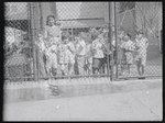 Children behind playground fence with teacher