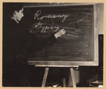Roma man writing “Romany” and “Gypsy” on a blackboard