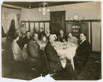 Group portrait showing Arthur Schomburg seated at head of table on far left with artist William Edouard Scott (fourth from left in background) and others