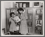 Librarian Augusta Baker showing a copy of Ellen Tarry's "Janie Belle" to a young girl at the library