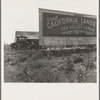 Camp of migrant agricultural workers along the highway in California. This signboard is used as a windbreak