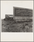 Camp of migrant agricultural workers along the highway in California. This signboard is used as a windbreak