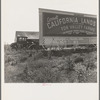 Camp of migrant agricultural workers along the highway in California. This signboard is used as a windbreak