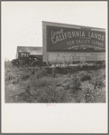 Camp of migrant agricultural workers along the highway in California. This signboard is used as a windbreak