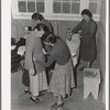 Camper receives help in fitting a coat from Works Progress Administration (WPA) sewing instructor. Shafter camp for migratory agricultural workers (Farm Security Administration-FSA), California