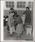 Camper receives help in fitting a coat from Works Progress Administration (WPA) sewing instructor. Shafter camp for migratory agricultural workers (Farm Security Administration-FSA), California