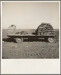 Kern County, California. Supply of fertilizer and potato seed on edge of field in which mechanical potato planter is operating