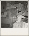 Mrs. Hull in one-room dugout basement home (note blackboard.) "I wanted a blackboard for a long time for my Bible verses, to keep them in our mind. Got it last year." Dead Ox Flat, Malheur County, Oregon. General caption number 67-111