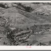 Looking down on Ola self-help co-op mill showing the upper end of Squaw Creek Valley, the creek lined with trees, the new dry shed near the mill, homes of co-op members and cultivated surrounding fields. Gem County, Idaho