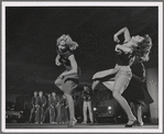 Three female dancers perform a step, while in the background male dancers as the Jets assume a menacing pose in a scene from the film version of West Side Story