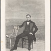 Portrait of a man, hand on second chair in front of studio backdrop