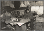 Buckboard Charlie reading the American Legion monthly in the living room of his shack near Iron River, Michigan