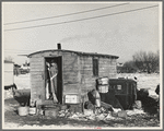 Mrs. Charles Benning sweeping steps of shack in "Shantytown," Spencer, Iowa