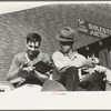Fruit auctioneer and clerk eating peaches in front of livestock pavilion, Sikeston, Missouri