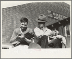 Fruit auctioneer and clerk eating peaches in front of livestock pavilion, Sikeston, Missouri