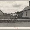 Man wheeling milk cans on board walk, Cook, Minnesota