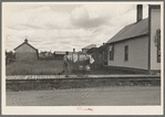 Man wheeling milk cans on board walk, Cook, Minnesota
