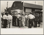 Groups of people standing in front of weighing concession with owner trying to drum up trade, state fair, Donaldsonville, Louisiana