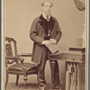 Full-length portrait of Charles Dickens, standing at desk, clasping book in both hands