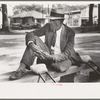 Crippled man sitting on bench in front of courthouse, Abbeville, Louisiana