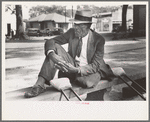 Crippled man sitting on bench in front of courthouse, Abbeville, Louisiana