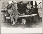Son of white migrant sitting on bumper of their truck, Weslaco, Texas. Notice New Mexico license