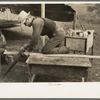 White migrant worker sawing wood for stakes to be used in setting up tent home, near Harlingen, Texas