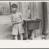 Mexican boy in front of community water hydrant and sink, San Antonio, Texas