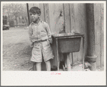 Mexican boy in front of community water hydrant and sink, San Antonio, Texas