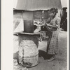 Mexican woman building fire in battered steel drum in backyard of her house, San Antonio, Texas