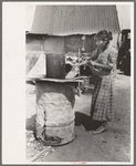Mexican woman building fire in battered steel drum in backyard of her house, San Antonio, Texas