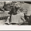 Wife of migrant auto wrecker sewing seat cushion of wrecked auto, Corpus Christi, Texas