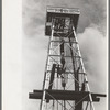 Top of derrick showing gin pole, crow's nest, crown block, traveling block, elevator and cat line. Oil well, Kilgore, Texas