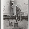 Day laborer filling five gallon cans with gasoline for use in tractors, large farm near Ralls, Texas