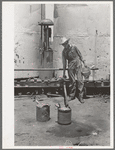 Day laborer filling five gallon cans with gasoline for use in tractors, large farm near Ralls, Texas