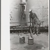 Day laborer filling five gallon cans with gasoline for use in tractors, large farm near Ralls, Texas