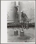 Day laborer filling five gallon cans with gasoline for use in tractors, large farm near Ralls, Texas