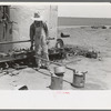 Day laborer filling five gallon cans with gasoline for use in tractors, large farm near Ralls, Texas