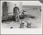 Day laborer filling five gallon cans with gasoline for use in tractors, large farm near Ralls, Texas