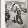 Day laborer pumping up tractor tire, farm near Ralls, Texas