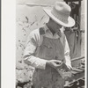 Day laborer looking through box of nuts and bolts, farm near Ralls, Texas