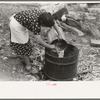 Spanish-American FSA client client emptying pail of grease into kettle for purpose of making soap, Taos County, New Mexico