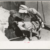 Seventy-five-year-old Spanish-Aamerican woman taking loaf of bread to place in outdoor earthern oven for baking, Taos County, N.M
